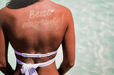 Sonnengebräunter Rücken einer Frau auf dem "Besser eincremen!" steht
